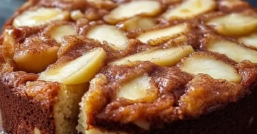 Leckerer Apfel Zimt Kuchen auf einem Teller serviert, mit Zimtstangen und Äpfeln dekoriert.