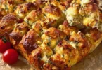 Zupfbrot mit getrockneten Tomaten, Feta und Mozzarella auf einem Holzbrett