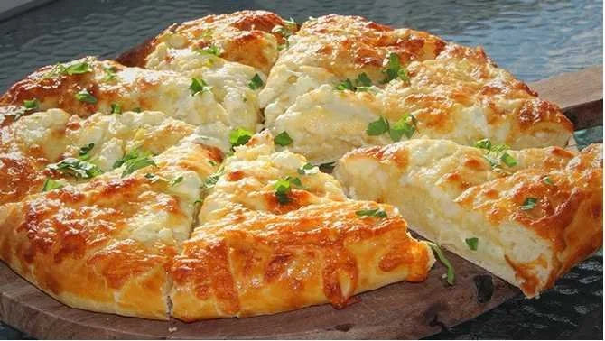 Leckeres Griechisches Käsebrot mit Feta und Kräutern auf einem Holzbrett.