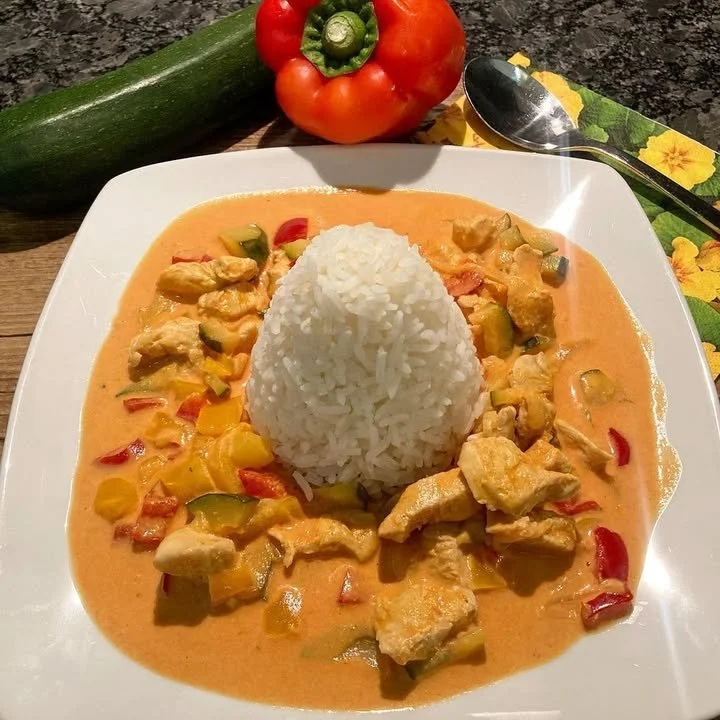 Paprika-Zucchini-Sahne Hühnchen serviert mit dampfendem Reis