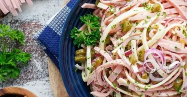 Schweizer Wurstsalat mit Käse und Gewürzgurken auf einem Teller angerichtet.