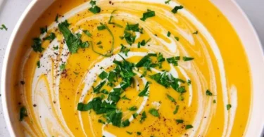Schüssel mit frischer Kartoffel-Möhren-Suppe, serviert mit frischen Kräutern