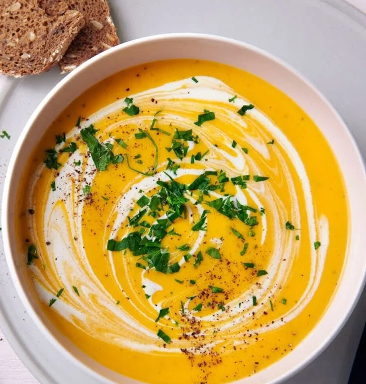 Schüssel mit frischer Kartoffel-Möhren-Suppe, serviert mit frischen Kräutern