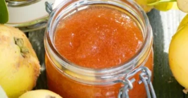 Quittenmus in einem Glas, serviert mit frischen Quitten und einem Löffel