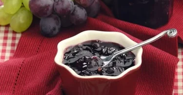 Glas Traubengelee auf einem Holztisch mit frischen Trauben.
